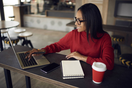 熟练的美国自由职业者在笔记本电脑上搜索项目浏览网页的信息，成功的深色皮肤的文案在社交网络中聊天，在坐在咖啡馆的笔记本电脑上打字