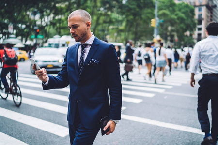 一位英俊的男经理穿着西装步行在市中心通过智能手机阅读新闻照片