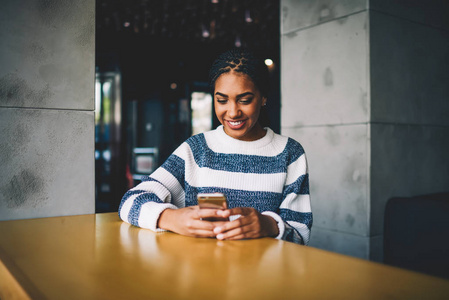 美丽的非洲美国时髦女孩穿着休闲装，坐在咖啡店里，通过免费的高速互联网连接在社交网络上与朋友聊天。
