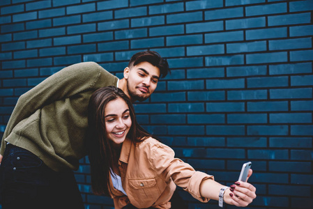 恋爱中的情侣们一起玩，一起在智能手机相机上拍照，在墙宣传背景，最好的朋友摆姿势自拍，在社交网络中博客，享受户外的空闲时间