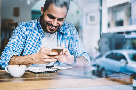 快乐的潮人笑着读着关于在咖啡厅休息的智能手机上赢得在线比赛的信息，快乐的男性在电话里收到好消息兴奋地读着短信享受着咖啡