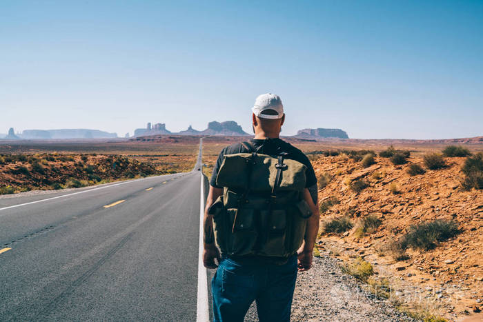 年轻的嬉皮士背着背包走在柏油路附近到西南国家公园男性旅行者搭便车