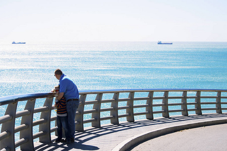 春天，男孩和他的父亲在西班牙的一座桥上看着大海