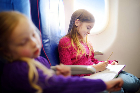 可爱的小女孩乘飞机旅行。 孩子坐在飞机窗前，用彩色铅笔画一幅画。 和孩子们一起出国旅行。