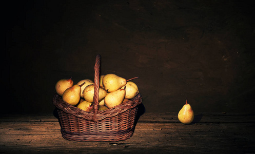 柳条篮子，在黑暗的背景上的木桌上放着梨。