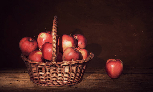 柳条篮子里有苹果和一个苹果在桌子上，黑暗的绘画背景。