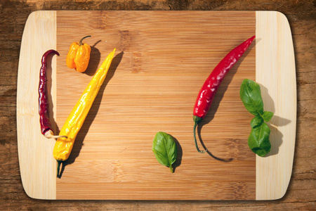 切板上的辣椒。 木制厨房板。 木头背景。 黄色哈巴内罗和新鲜罗勒叶。