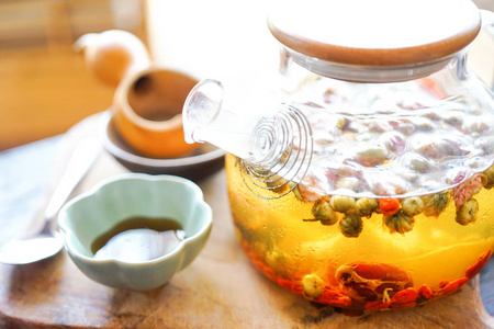 透明茶壶里的中国绿茶在木桌上。背景中，一个明媚阳光的早晨照亮了周围的一切..带有复制空间的特写视图
