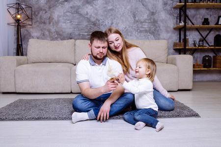 小女孩，她的父亲和母亲正在家里和小鸡玩耍，微笑着。金发可爱的女婴和她的家人坐在沙发附近的地毯上。家庭复活节庆祝活动