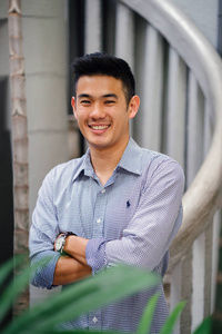 一位英俊年轻聪明的中国亚洲男人穿着西装，微笑着站在绿色的墙上。他有一头短发，穿着一套灰色的西装。