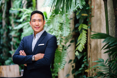 一位英俊,年轻,聪明的中国亚洲男人穿着西装,微笑着站在绿色的墙上.