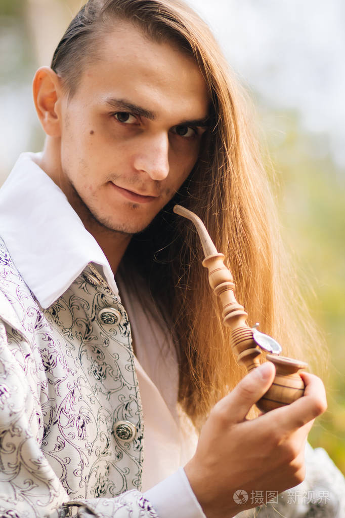 性感的长发男人,手里拿着烟斗在树林里.