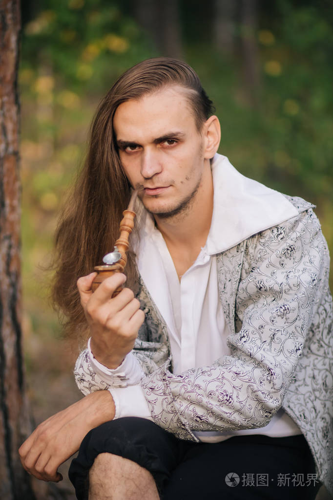 性感的长发男人,手里拿着烟斗在树林里.