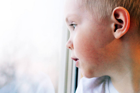 可爱的小金发碧眼的男孩坐在窗边, 所以伤心