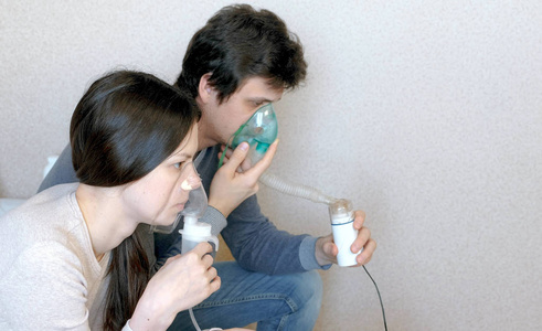 使用喷雾器和吸入器进行治疗。男人和女人吸入吸入口罩。特写侧面视图