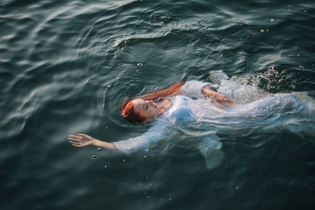 水的幻想美丽的红头发女孩漂浮在水中. 岩石海岸.
