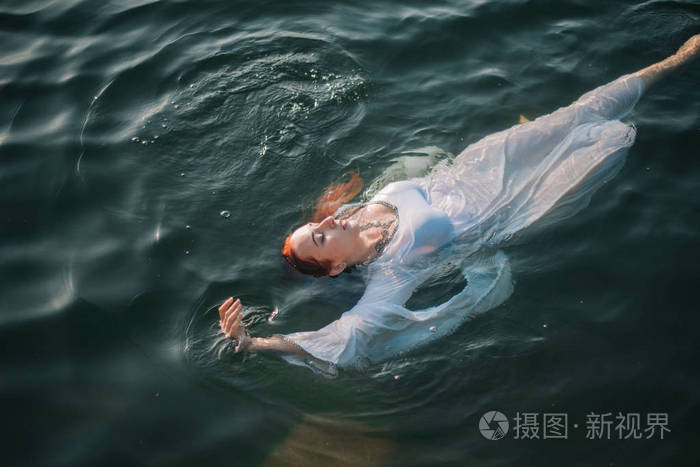 美丽的红发女孩漂浮在水中洛基海岸穿着一件白色古色