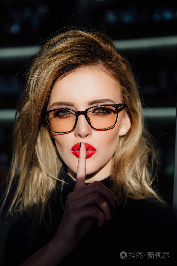 戴眼镜的女人要求用手指在红唇上保持沉默或保密.嘘手势