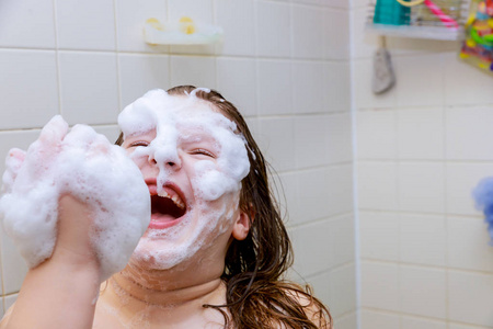 小女孩在浴室洗脸，快乐的小女孩用手吹泡沫。