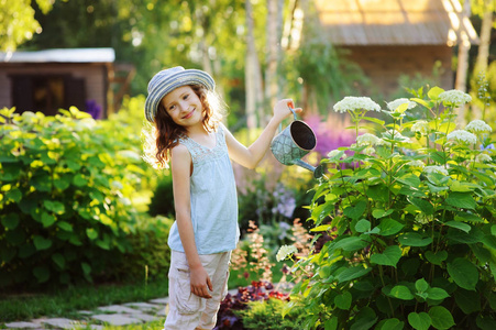 快乐的孩子在阳光明媚的夏日花园里扮演小园丁和浇水绣球花，小帮手的概念。孩子们在乡下度过暑假。