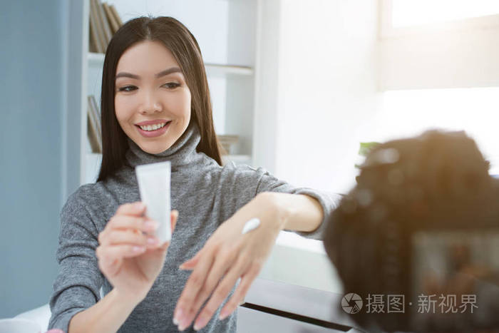 年轻的博主正在向相机展示她最喜欢的美容产品.它是用手霜的管子