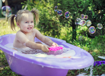 夏天在花园里，一个小女孩在塑料浴缸里洗澡，里面有玩具肥皂泡。