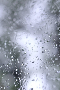 一张雨滴在窗户玻璃上的照片，模糊地看到了盛开的绿色树木。 显示阴天和雨天天气情况的抽象图像