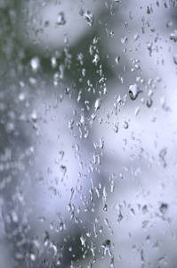 一张雨滴在窗户玻璃上的照片，模糊地看到了盛开的绿色树木。 显示阴天和雨天天气情况的抽象图像