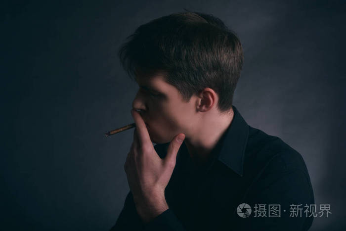 男人在抽雪茄. 男孩在黑暗的背景上抽烟.