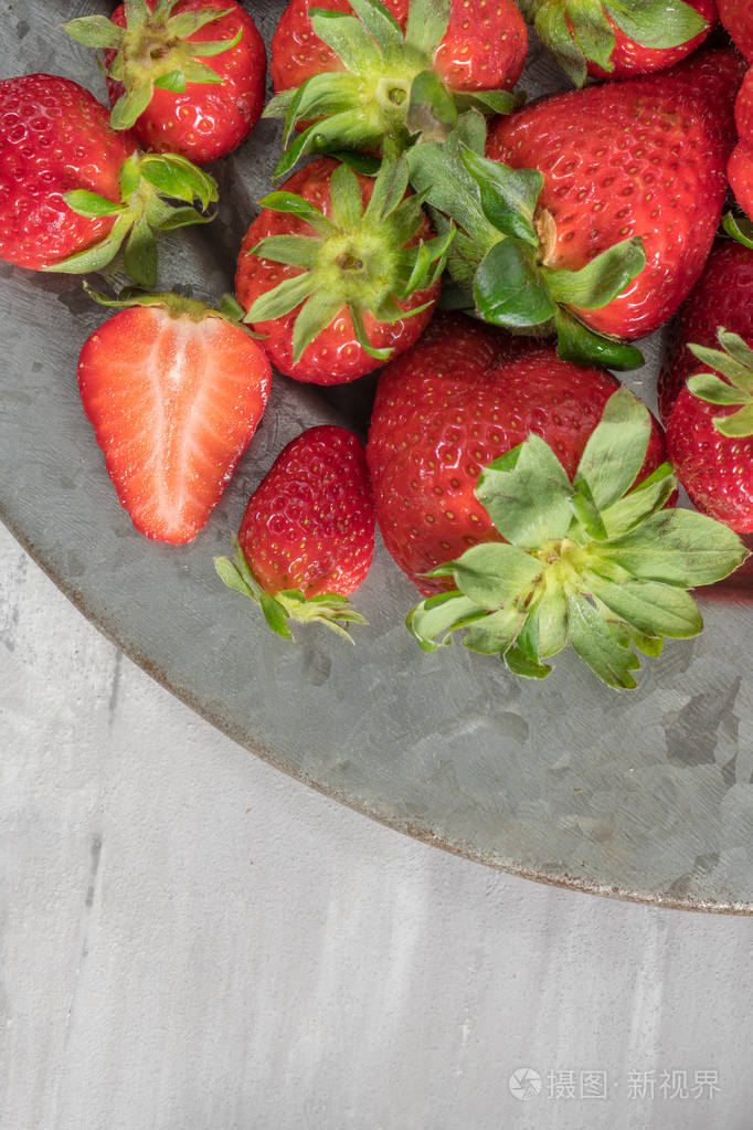 在水泥背景下装满新鲜草莓的盘子.生草莓