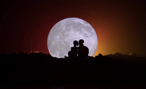 在满月下亲吻情侣的剪影.男孩亲吻女孩手在满月剪影背景.