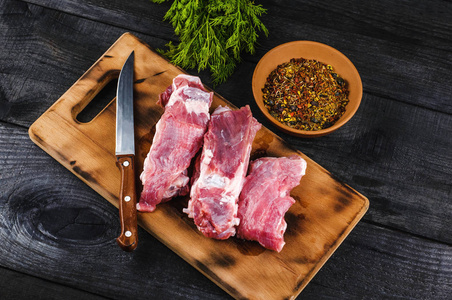 新鲜的生牛肉排骨在切割板上，刀香料和欧芹在黑色的木制背景上。