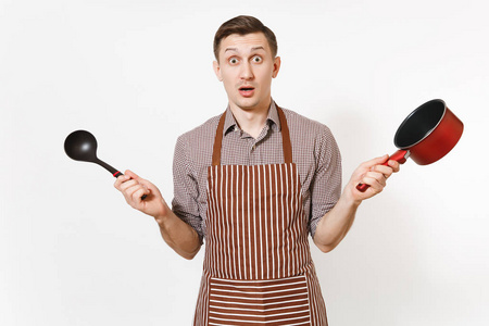年轻的男子厨师或服务员在条纹棕色围裙, 衬衫持有红色空 stewpan 黑钢包孤立的白色背景。男管家或 houseworker。