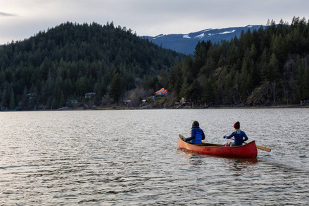 在一个充满活力的日落中，木制独木舟上冒险的人正在欣赏美丽的加拿大山景。 摄于加拿大不列颠哥伦比亚省温哥华以东的哈里森河。