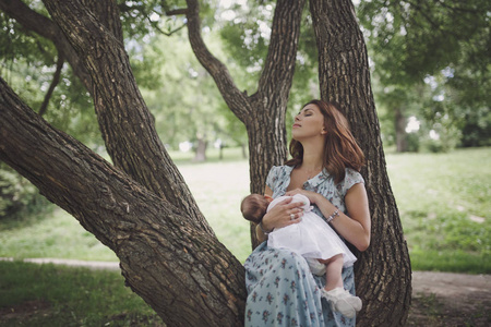 哺乳女人一个美丽的微笑的年轻黑发女人,长发正在哺乳一个漂亮的婴儿.