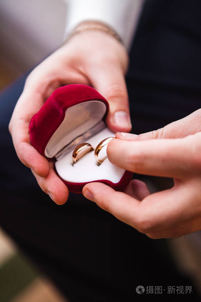 新郎手里拿着一个天鹅绒礼品盒里面有一颗带结婚戒指的心