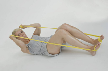 年轻女子躺在她的背上,挽着一条裹在她脚上的黄色体操丝带照片