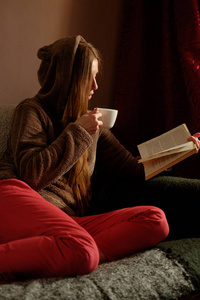 红发姜女孩在滑稽的 hoody 读书, 喝咖啡