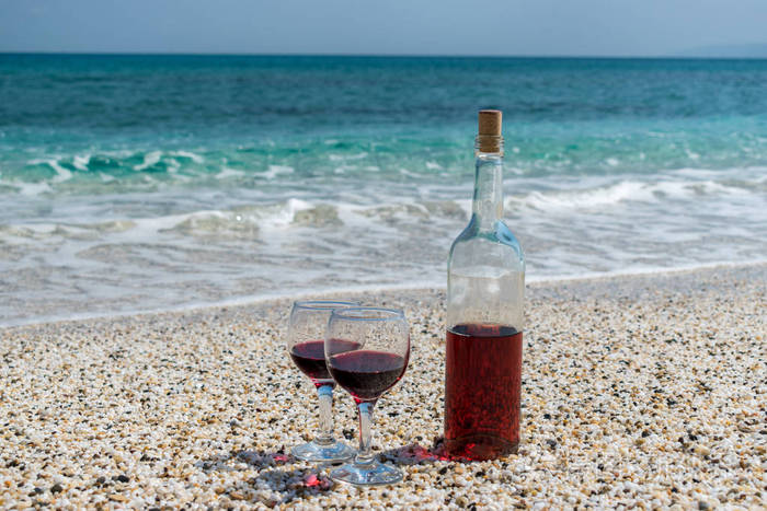 夏日阳光明媚的日子海滩上的红酒和瓶子的酒杯
