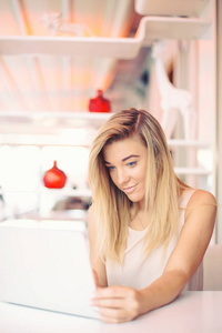 一个美丽的年轻的微笑的女商人在早上在一个舒适的咖啡馆工作的笔记本电脑