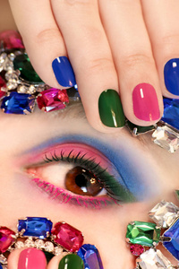 时尚的彩色短指甲艺术设计在女性手上，与装饰在脸上。指甲艺术。蓝色绿色粉红色指甲油。流行美甲。多种颜色的化妆设计和风格的美丽指甲。