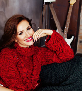 年轻漂亮时尚的女人穿着红色的冬天毛衣在家里的沙发里，快乐的微笑的生活方式，人们的概念接近。