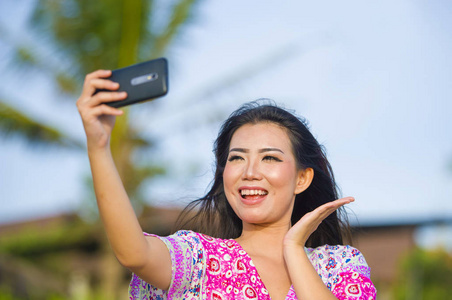 愉快的美丽和华丽的亚洲中国妇女在魅力礼服采取自画像自拍照片与移动电话在假日热带度假胜地