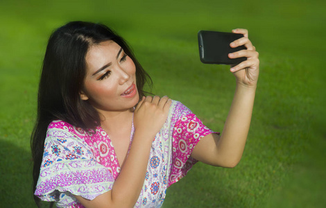 年轻的快乐和美丽的亚洲华人妇女采取自拍 pic 与手机相机摆在草地上的感官和嬉戏的户外草坪公园