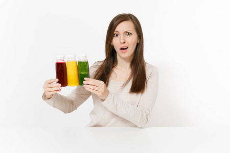 在餐桌上的年轻妇女与绿色, 红色和黄色的排毒冰沙酒瓶在白色背景隔离。适当的营养, 素食饮料, 健康的生活方式, 节食的概念。具有