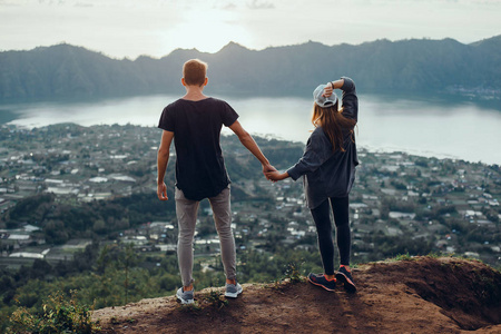 情侣旅行者男女坐在悬崖上放松的山和云,鸟瞰爱情和旅行快乐的情感