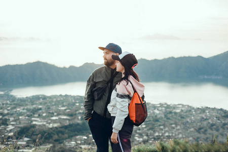 情侣旅行者男女坐在悬崖上放松的山和云，鸟瞰爱情和旅行快乐的情感生活理念。 年轻家庭旅行积极冒险度假者