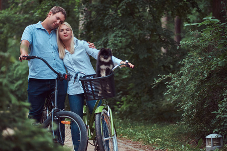 一对迷人的夫妇，一男人拥抱着穿着休闲服的自行车骑行，他们可爱的小斯皮茨在篮子里。