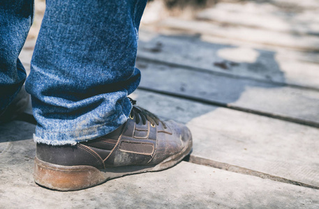 在木桥上穿着泥土运动鞋特写的男性腿