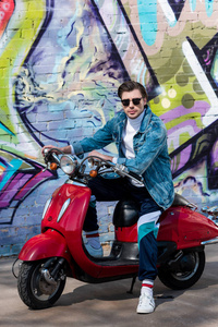 有魅力的年轻人骑着老式红色滑板车在砖墙前涂鸦